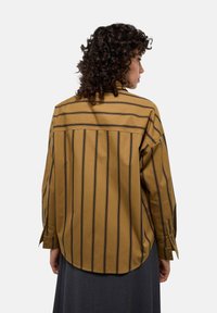 Chemise à manches longues de couleur jaune moutarde avec des rayures verticales noires, dotée d'un ourlet arrondi et de poignets à boutons. Texture lisse, design décontracté.
