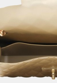 Interno della borsa a tracolla beige trapuntata con una base liscia e strutturata. Presenta una chiusura in metallo dorato e una silhouette arrotondata.