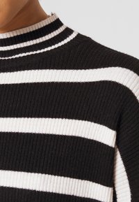 Zbliżenie na prążkowany czarno-biały sweter z golfem noszony przez osobę, z naciskiem na obszar ramion i szyi.