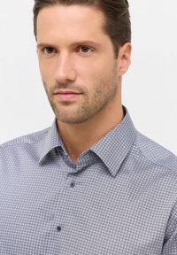 Overhemd met knoopsluiting in een geometrisch patroon, met een spread collar, korte mouwen en donkere knopen. Kleurencombinatie omvat wit en marineblauw.