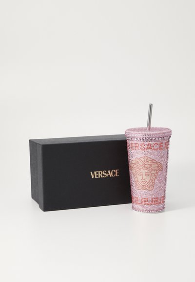 Versace vaaleanpunainen koristeltu kuppi hopealla pillillä, jossa on monimutkainen helmityö ja brändin logo, esitelty mustassa laatikossa.