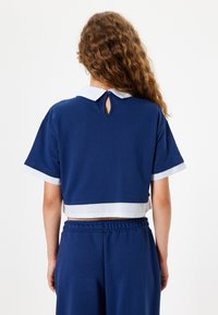Lyhyet hihat ja tummansininen croppitoppi, jossa on vaaleansininen ja valkoinen raidallinen kaulus sekä takana avainaukko, valmistettu pehmeästä kankaasta.