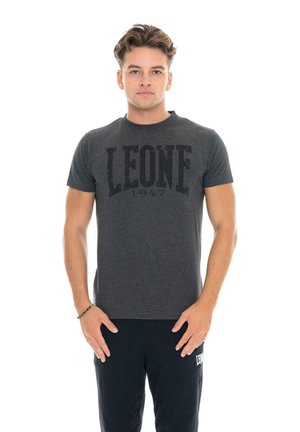 Un homme porte un T-shirt Leone 1947 gris foncé et un pantalon noir sur un fond blanc uni.