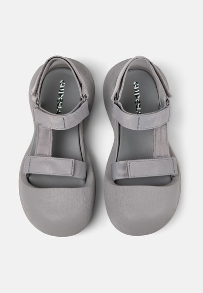 Gray sandals with a smooth, matte texture, featuring adjustable straps and a rounded toe design, with a padded interior for comfort.
