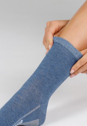 Blauer Socken aus weichem Stoff, mit einem gerippten Bündchen, glatter Textur und verstärktem Absatz. Hand, die den Socken hochzieht.