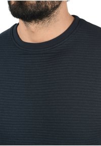 Sudadera texturizada de color azul marino con un patrón de canalé y un cuello redondo. La tela parece suave y ligeramente elástica.