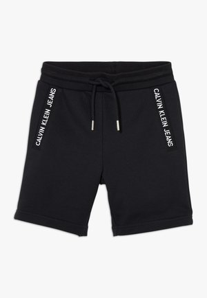 Sorte Calvin Klein Jeans shorts med elastik i taljen, snøre og hvid logo tekst på sidelommerne mod hvid baggrund.