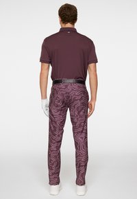 Bordo polo z krótkim rękawem, w połączeniu z spodniami w konturowym wzorze w purpurowym i białym kolorze. Uzupełnione czarnym paskiem i białymi rękawiczkami.