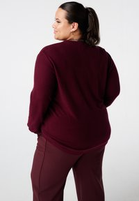 Bordeaux pullover van zachte stof, met een relaxed fit en lange mouwen. Gecombineerd met bijpassende bordeaux broek.