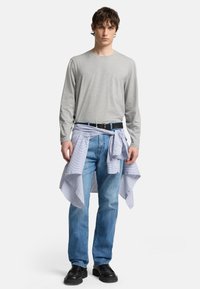 Maglietta grigia a maniche lunghe, jeans blu, cintura nera. Camicia a righe legata in vita. Scarpe nere. Outfit semplice e casual.