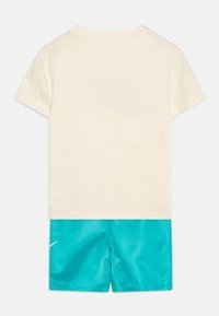 Kratka majica iz kremastega bombaža, v kombinaciji s turkiznimi kratkimi hlačami z belim Nike logotipom, gladka tekstura in lahka zasnova.