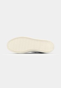 Shoe sole in white rubber with a zigzag pattern, featuring a smooth texture and rounded edge. Designed for grip and flexibility.