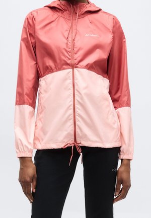 Kvinde iført en todelt pink Columbia hættetrøje med lynlås og snøre i taljen samt sorte bukser.