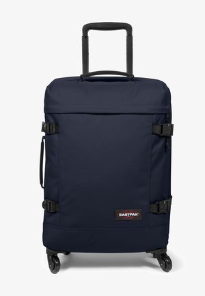 Valise à roulettes en tissu bleu marine, dotée d'une poignée rétractable, de deux sangles de fixation et de roues pour la mobilité. Comprend un écusson logo à l'avant.