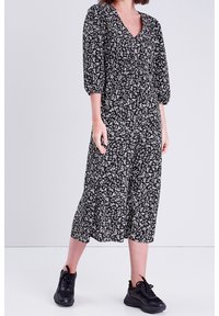 Robe noire avec imprimé floral blanc, décolleté en V, manches 3/4, taille élastique, jupe fluide se terminant au milieu du mollet. Associée à des baskets noires.