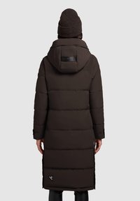 Brun pufferjakke med hætte, der har en quiltet design, skulderpatch-logo og sideslids for nem bevægelse.