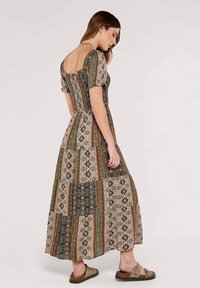 Robe maxi avec un design en patchwork comportant des motifs verts, orange et crème. Les manches bouffantes et le dos ouvert ajoutent des détails. Tissu doux.