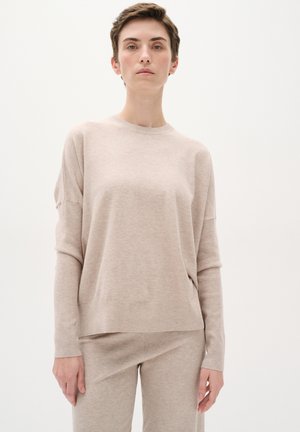 Pull en tricot beige à la coupe décontractée, col rond, manches longues et côtes discrètes à l'ourlet. À associer avec un pantalon beige assorti.
