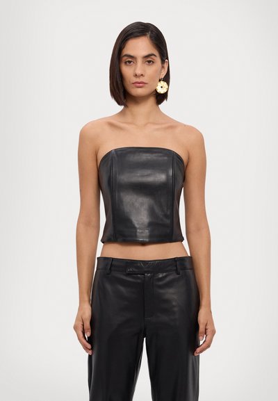 Top court sans bretelles en cuir noir avec une finition lisse et un design structuré. Associé à un pantalon en cuir noir taille haute.