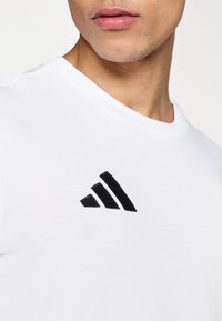 Λευκό βαμβακερό κοντομάνικο μπλουζάκι με μαύρο κεντημένο λογότυπο με τρεις διαγώνιες ρίγες στην αριστερή πλευρά του στήθους.