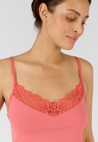 Top camicia corallo con un delicato pizzo lungo il colletto, sottili spalline regolabili e una trama liscia e morbida.