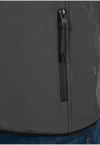 Graue Jacke mit einer seitlichen Reißverschlusstasche und schwarzem Reißverschluss. Das Material hat eine glatte Textur, und das Design umfasst eine elegante, moderne Passform.