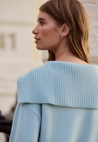 Gaiši zils džemperis ar plata, ribotu apkakli un mīkstu tekstūru. Demonstrē vaļīgu siluetu, ar garām piedurknēm un gludu apdari.