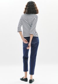 Randig långärmad tröja med rundad halsringning och asymmetrisk baksida, kombinerad med mörkblå avsmalnande jeans och svarta slip-on skor.