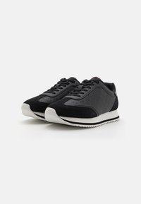 Chaussures de sport noires en tissu texturé et en daim, avec une semelle en caoutchouc blanche et des lacets noirs, au design élégant et profil bas.