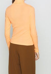 Langärmliges, Rollkragenoberteil aus leicht orangefarbenem Rippstoff, kombiniert mit braunen, weiten Hosen. Glatte Textur, figurbetontes Design.