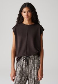 Donkerbruin t-shirt met korte mouwen en een ronde halslijn, gecombineerd met lichtbeige en zwarte, geprinte broek met een elastische tailleband.