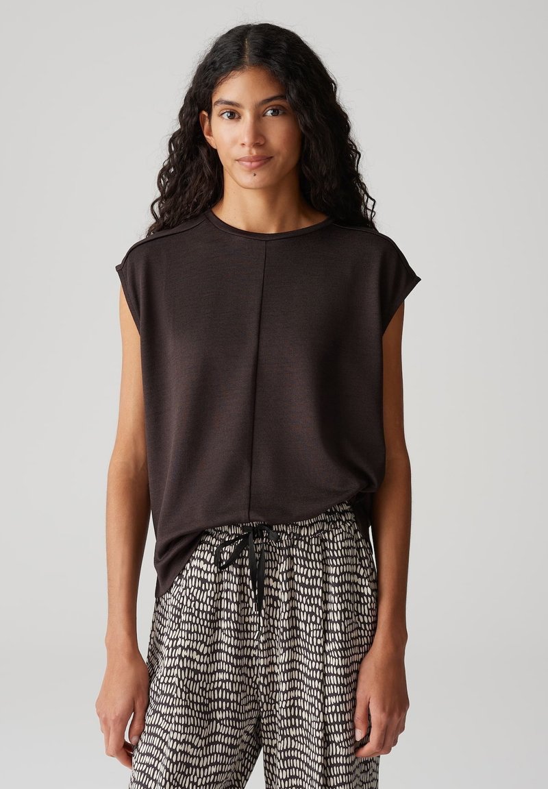 Donkerbruin t-shirt met korte mouwen en een ronde halslijn, gecombineerd met lichtbeige en zwarte, geprinte broek met een elastische tailleband.