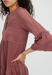 Robe à manches froncées en rose poussiéreux, ornée de motifs en dentelle complexes, d'un col à boutons et d'une jupe évasée et à volants.