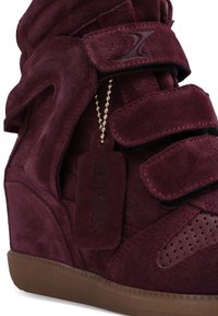 Καστανό σουέντ πλατφόρμα sneaker με λουριά βέλκρο, διάτρητη περιοχή στη μύτη, λογότυπο σουέντ σε χρυσή αλυσίδα με σφαιρίδιο και καφέ καουτσούκ σόλα.