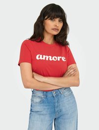 Rød bomulds t-shirt med hvid "amore" tekst, med en rund halsudskæring. Sammen med lyseblå højtaljede jeans.