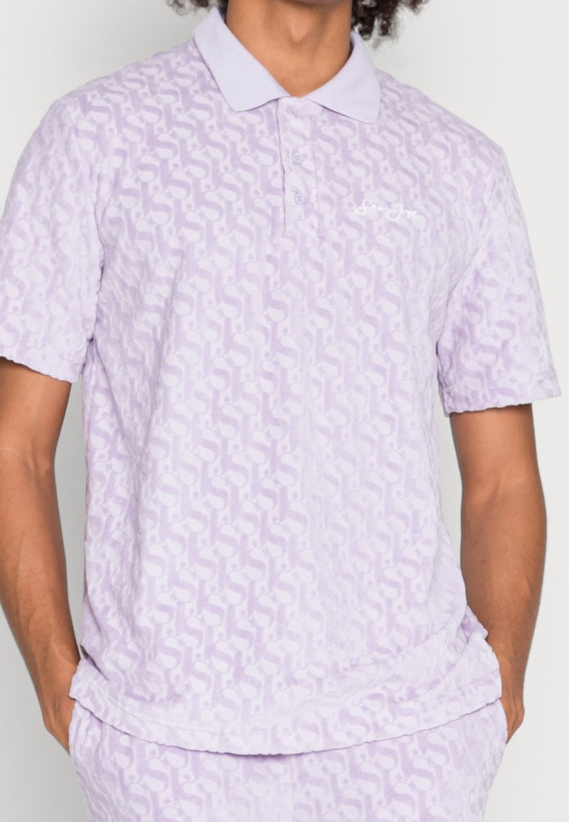 Polo shirt lavande à manches courtes, en tissu texturé avec un motif subtil, et un col classique. Logo de la marque brodé sur le devant.