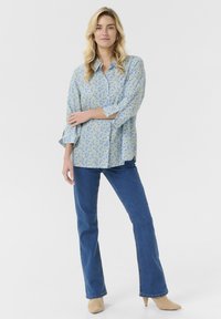 Camicia a maniche tre quarti blu chiaro a fiori, abbinata a jeans a zampa d'elefante blu e tacchi beige. Tessuto morbido, vestibilità rilassata.