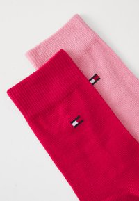 Røde og rosa bomullssokker med ribbet design, med en logo-patch i rødt, hvitt og svart på kanten av den røde sokken.