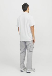 Hvid kortærmet t-shirt, grå cargo bukser med flere sidelommer, iført sølvfarvede sneakers, set fra ryggen.
