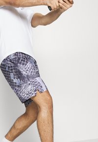 Korta, atletiska shorts i ett flerfärgat mönster med rutor och texturer i nyanser av lila och svart, med ventilerade fållar.