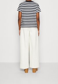 Stribet navy og hvid t-shirt med korte ærmer, parret med vide hvide bukser og brune block-heeled sko. Minimalistisk design.