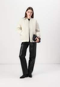 Beige-vuorattu bomber-takki, musta istuva paita, korkeavyötäröiset mustat nahkahousut ja mustat korkokengät nilkkureilla. Musta clutch-laukku.