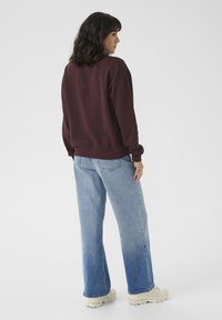 Bordeauxfarbenes Baumwoll-Sweatshirt mit langen Ärmeln und gerippten Bündchen, kombiniert mit hellblauen, weiten Denim-Jeans und weißen Sneakers.