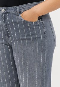 Jeans de denim cinza com embellishments prateados verticais, um bolso frontal e um design clássico de cinco bolsos.