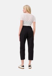Zwarte high-waisted broek met een tapered leg ontwerp, zijzakken en achterzakken, gecombineerd met een witte slim fit t-shirt en casual sneakers.