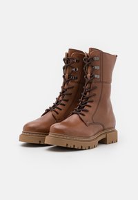 Hnědé kožené šněrovací boty s kulatou špičkou, polstrovaným límcem a robustní gumovou podrážkou; obsahují kovové nýty a detaily šití.