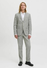Traje gris claro con un acabado texturizado, que incluye un blazer de un solo botón, pantalones a juego y zapatos de cuero negro. Camisa blanca debajo.