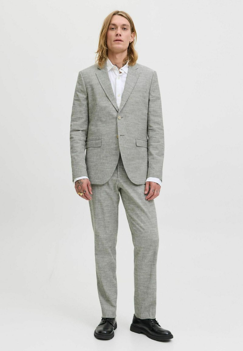 Traje gris claro con un acabado texturizado, que incluye un blazer de un solo botón, pantalones a juego y zapatos de cuero negro. Camisa blanca debajo.
