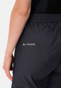 Pantalons Vaude noirs avec une taille élastique. Tissu lisse et léger avec un léger éclat. Logo imprimé en blanc sur le côté.