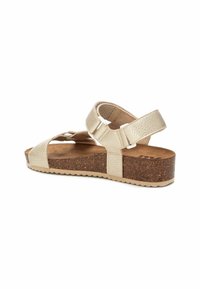 Sandalia beige con correas texturizadas, hebillas ajustables y una suela de corcho. Presenta una puntera redonda abierta y una parte inferior de goma con relieve.